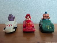 Front view of three character cars: white Grimace, red Ronald, green Mayor McCheese