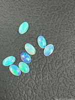 Eight oval opal cabochons on textured dark surface showing play of color
