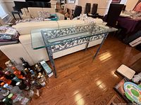 full front view of console table showing glass top and ornate iron base
