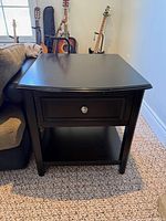 Front view of first black side table, showing drawer, knob, shelf