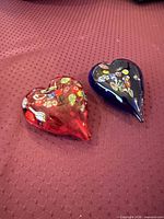 Red and blue Murano glass heart paperweights side by side