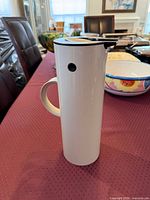 Full side view showing cylindrical form, handle, rocker lid