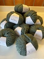Pile of ten sage green bulky yarn balls with labels visible