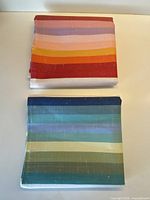 Two folded tea towels showing their distinct warm and cool stripe palettes