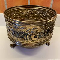 full view of brass planter showing repousse decoration and claw feet