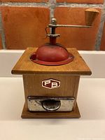 Front view showing PB badge, metal drawer, red dome lid, crank