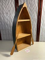 Front view of boat-shaped shelf showing three tiers and oars