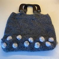 Full view of felted wool bag front showing color, shape, wood handles, decorative spheres
