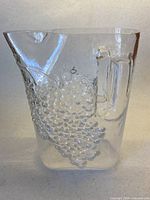 Full view of clear glass pitcher with grape cluster relief and handle