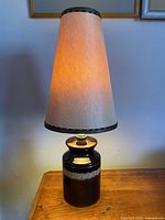 Full view of ceramic lamp with shade illuminated on wooden surface