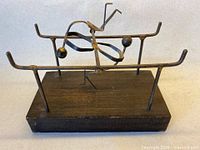 Front view of metal balancing sculpture on wood base showing overall structure