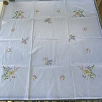 Full view of white linen tablecloth laid flat showing overall embroidery layout and hemstitched border