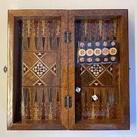 board opened showing inlaid backgammon field, sealed checkers pack and dice