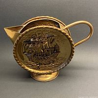 front view showing repousse ship motif, handle, spout