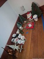 All items arranged on floor: mugs, Santa cookie jar, wooden trees, glass dish, star topper, wood decor, snowman container