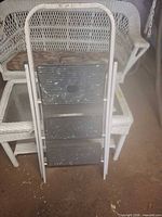 Front view of folded three-step metal stool showing frame and treads