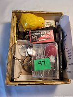 Top view of cigar box showing toy chick, Medico packet, eyeglasses, hair pins, coin and misc smalls