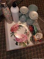 Box containing water bottles, plastic wine glasses, melamine plates, bag of kitchen utensils