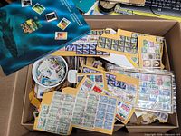 Overview of box showing envelopes, stock sheet pieces with stamp blocks and a stamp album cover