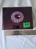 Top view showing purple mirrored lid with jeweled decoration and ruler for scale