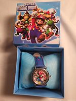 Open box showing watch on cushion, full view of dial and strap