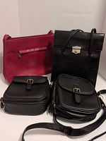 Group shot showing all four bags: Roots black handbag, red leather bag, two small black purses