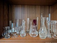 Shelf containing multiple clear glass bud vases of varying shapes and sizes