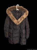 Front view of black down coat on hanger showing hood fur trim and quilting