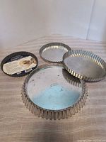 Stack of round tin tart pans with removable bases and a dark non-stick pan visible