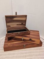 Stack of three cedar boxes, top box open showing black felt interior and cedar grain, latches visible