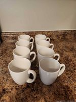 Front angled view showing all eight white mugs in a row