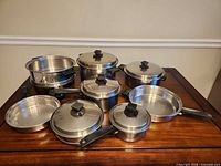 Full cookware set arranged on table showing all pots, pans, lids and steamer