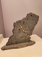 Front view of gray porous lava rock clock on stone base