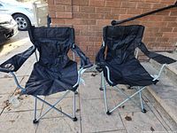 Two black folding camping chairs side by side unfolded on pavement