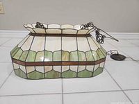 Front view of stained glass chandelier showing cream, green and amber panels and attached chain