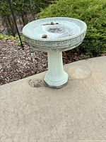 Full view of cast cement bird bath on patio showing bowl, pedestal, and weathered finish