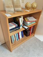 Front view of light wood veneer three-shelf bookcase with books inside (contents excluded)