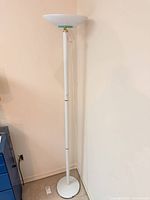 Full view of white torchiere floor lamp in corner showing bowl shade, pole, base