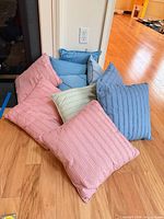 Group of ten square pleated pillows in assorted colors on hardwood floor