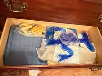 Drawer containing blue placemats, blue plastic candelabra parts, bag of yellow candles, package of white paper doilies