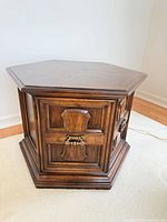 Front view of wood hexagon side table showing paneled doors and brass pulls