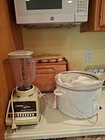 Blender, Crock-Pot, breadbox, pot holders grouped on countertop