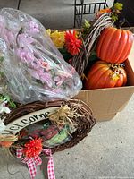 Box containing two orange pumpkins, grapevine wreath, loose faux flowers