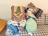 Pile showing tapestry urn throw, ivory throw, scenic pillow, blue round pillow