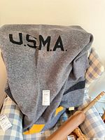Full view of gray wool blanket draped, showing black U.S.M.A. lettering and stripe detail