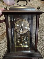 Front view showing wood case, glass panels, brass dial, rotating pendulum