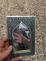 Front view of silver-tone metal mirror frame with Moorish arch opening and scrollwork border