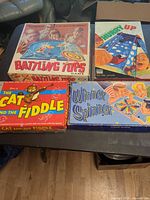 Four game boxes laid out on table: Battling Tops, Hurry Up, Cat and the Fiddle, Winner Spinner