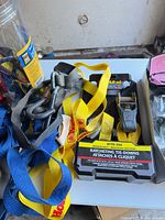 Yellow ratcheting tie-down strap, assorted blue and grey straps, jar edge visible