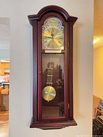 Full view of Bulova wall clock hanging on wall showing entire case and pendulum